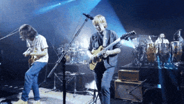 a man playing a guitar and another man playing a guitar on a stage