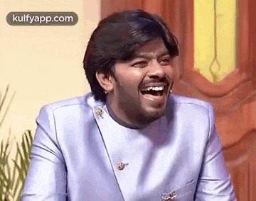 a man in a blue suit is laughing while sitting in front of a wooden door .