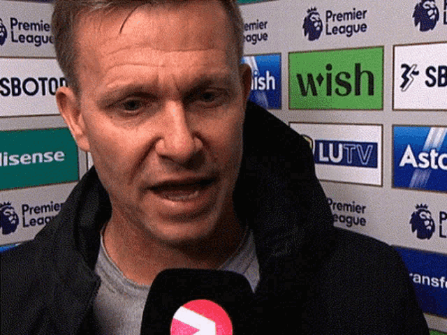 a man speaking into a microphone in front of a wall that says premier league on it