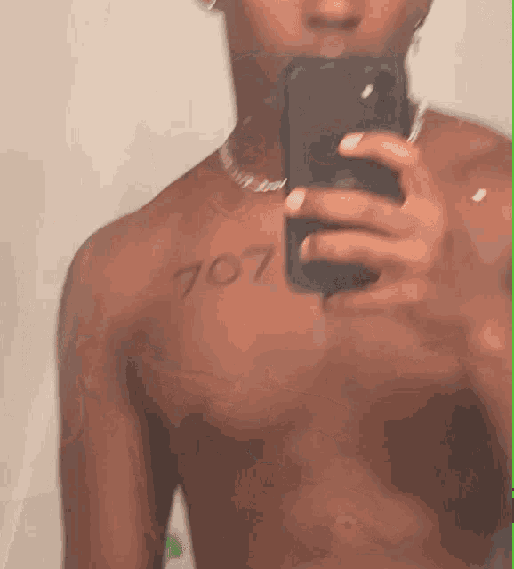 a shirtless man is taking a picture of himself with the number 707 on his chest