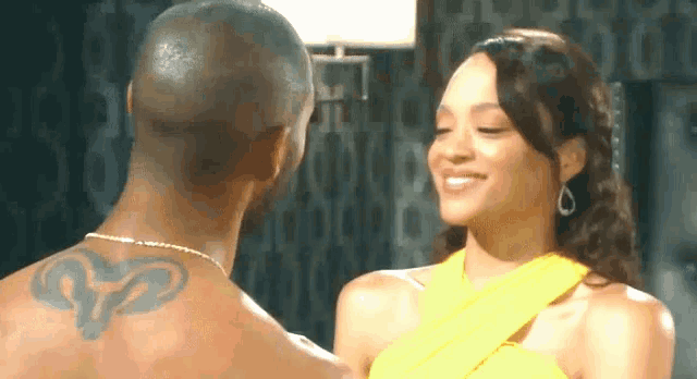 a woman in a yellow dress is smiling at a man with a tattoo on his back