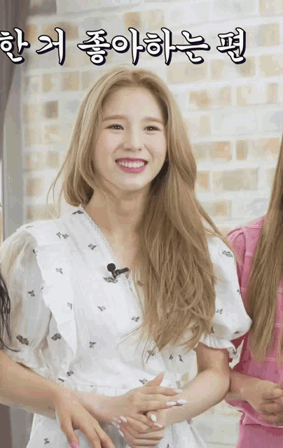 a woman in a white dress is smiling in front of a brick wall with korean writing on it