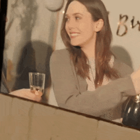 a woman is holding a glass of wine and smiling while looking at herself in the mirror .