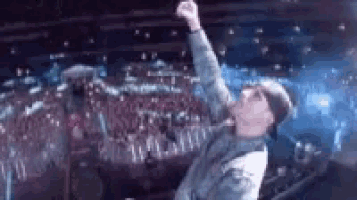 a man is standing on a stage with his fist in the air and a crowd behind him .
