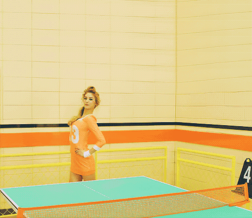 a woman in an orange shirt with the number 8 on it is playing ping pong