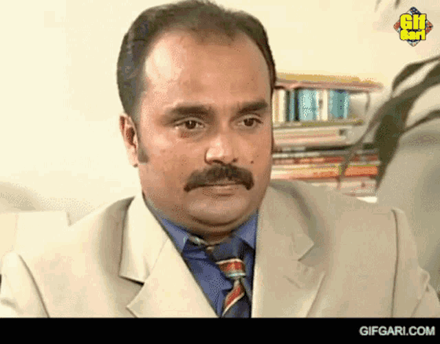 a man with a mustache is wearing a suit and tie with a gifgari.com logo on the bottom