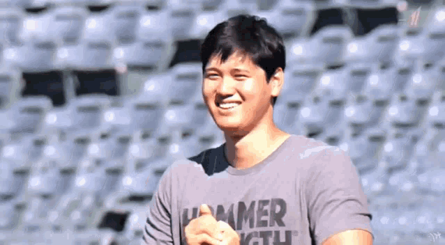 a man wearing a hammer youth t-shirt is standing in front of a stadium full of empty seats .