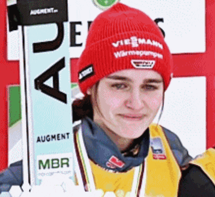 a woman wearing a red beanie and a yellow vest holds a ski