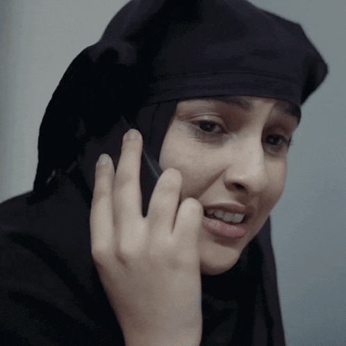 a woman in a black head scarf is talking on a cell phone