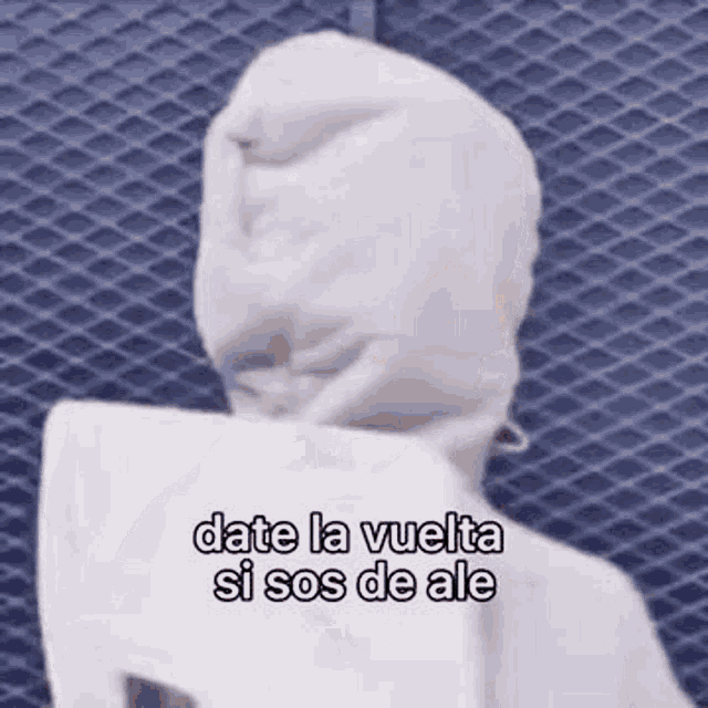 a person wearing a white hoodie with a hood is standing in front of a fence .