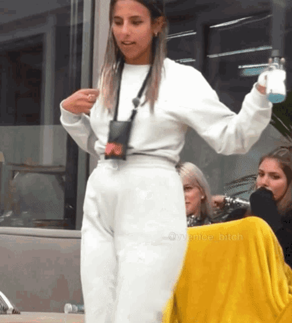 a woman in a white sweater and white pants is standing in front of a yellow blanket and a window