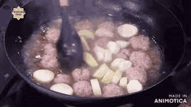 a pan filled with meatballs and vegetables is being stirred with a spatula .