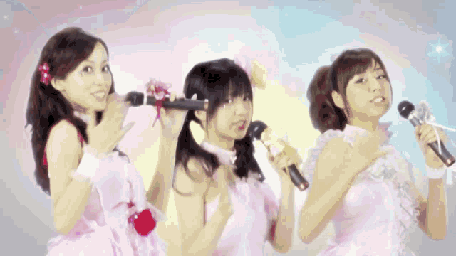 three women in pink dresses are singing into microphones and giving the thumbs up sign