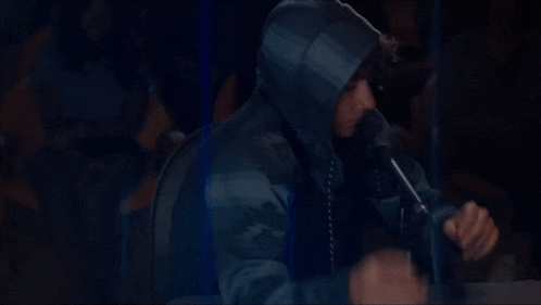 a man in a hooded jacket is singing into a microphone in front of a crowd