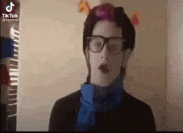 a woman wearing glasses and a blue scarf is standing in front of a wall .
