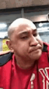 a man with a bald head is wearing a red shirt and a red jacket .