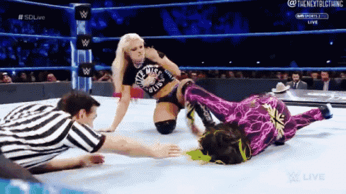 two women are wrestling in a wrestling ring with a referee watching