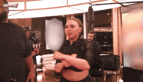 a woman in a black crop top is standing in front of a microphone and a sign that says now thats tv