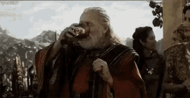a man with a beard is drinking from a glass while standing in front of a crowd of people .