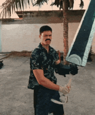 a man with a mustache is holding a large sword in front of a palm tree