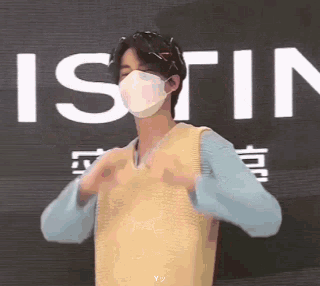 a young man wearing a mask and a vest is making a heart shape with his hands .