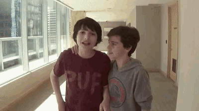 two young boys are standing next to each other in a hallway and laughing .