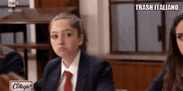 a girl in a suit and tie is sitting in a classroom with a sign that says trash italiano .