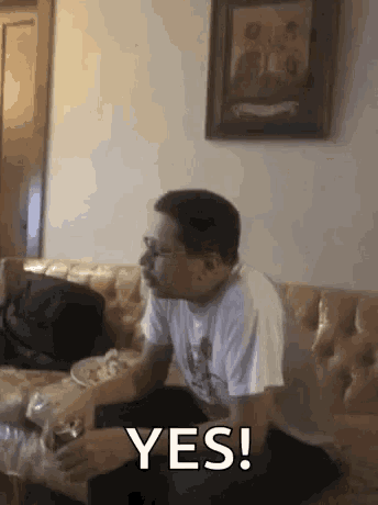 a man is sitting on a couch holding a glass of beer and says yes