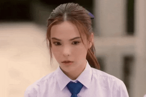 a young girl wearing a white shirt and blue tie is looking at the camera .