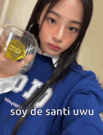a girl in a blue sweatshirt is holding a glass with the words soy de santi uwu written below her