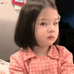 a little girl in a pink plaid shirt is sitting on a bed and looking at the camera .