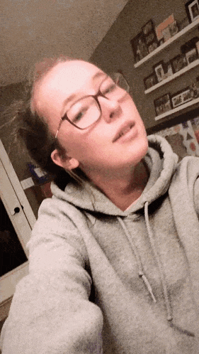 a woman wearing glasses and a grey hoodie looks at the camera