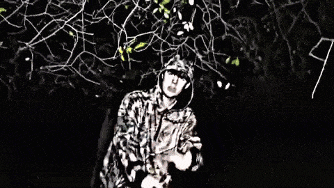 a man in a camo jacket is standing in a field with a tree in the background .