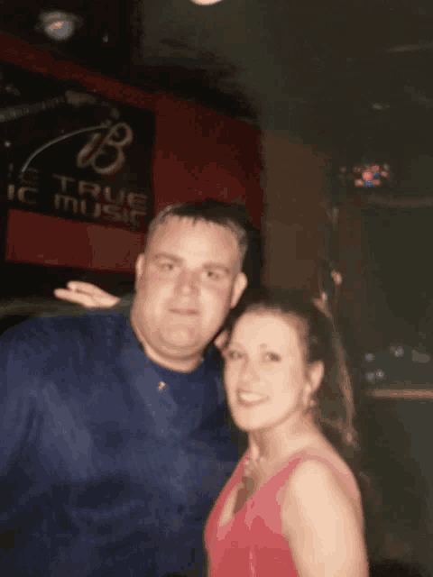 a man and a woman pose for a picture in front of a true music sign