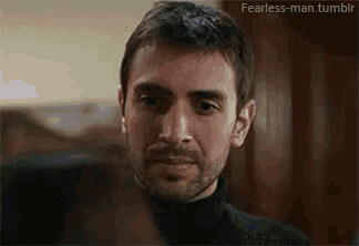 a man with a beard and a black turtleneck is looking at the camera .
