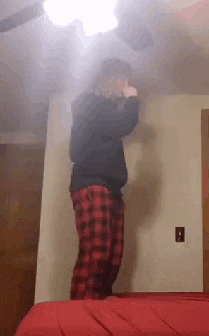 a man in plaid pajamas is standing on a bed in a room .