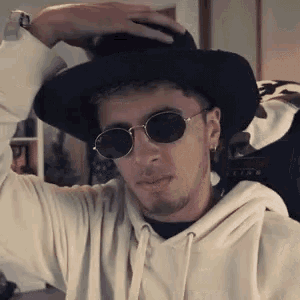 a man wearing a hat and sunglasses is holding his hat .