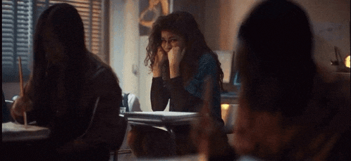 a woman is sitting at a desk in a classroom with her hand on her face .