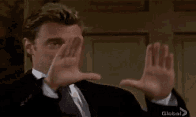 a man in a suit and tie is smiling and making a thumbs down sign with his hands .