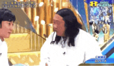 a man with long hair is talking to another man on a tv show .