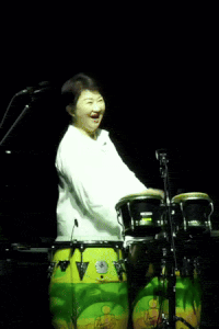 a woman in a white shirt is smiling while playing a drum set