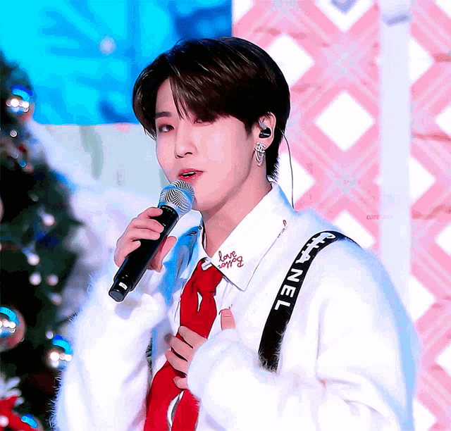 a young man singing into a microphone wearing a white shirt with chanel on it