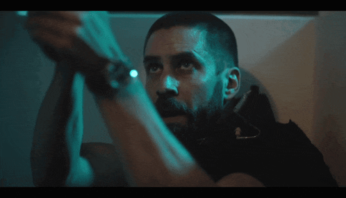 a man with a beard in a dark room with a blue light behind him