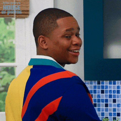 a man in a colorful sweater is smiling in front of a window with a house of payne logo