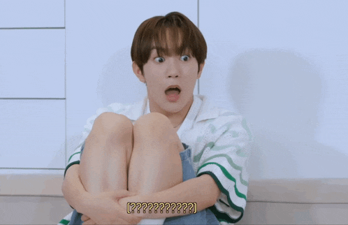 a young boy with a surprised look on his face is sitting on the floor with his legs crossed and the words [ ?? ] below him