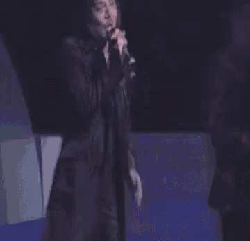 a man in a black jacket is singing into a microphone on a stage .