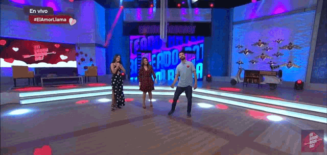 a man and two women are dancing on a stage in front of a sign that says " en vivo "
