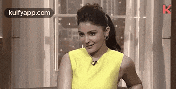 a woman in a yellow dress is sitting on a couch in front of a window .