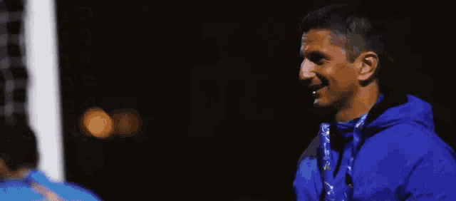 a man in a blue jacket with a medal around his neck stands on a soccer field