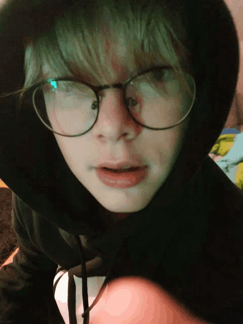 a person wearing glasses and a black hoodie looks at the camera